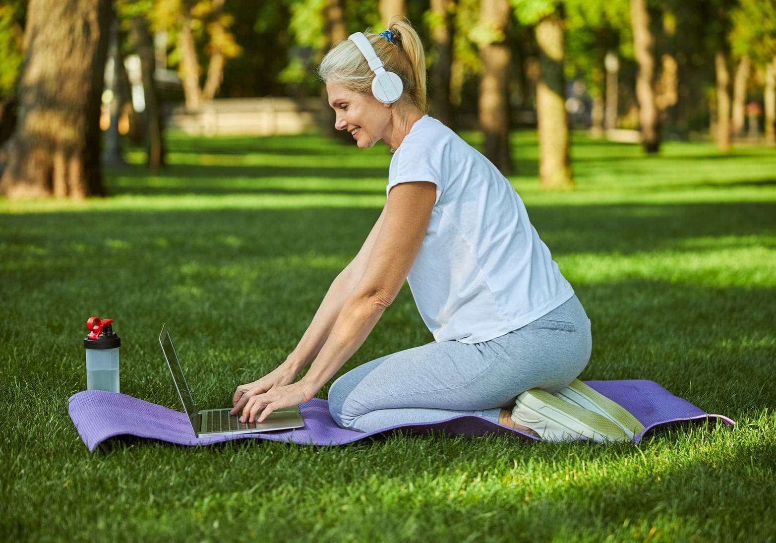 joyful-woman-in-headphones-using-notebook-in-park-2023-11-27-05-17-15-utc